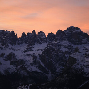 Nell'immagine si vedono le Dolomiti di Brenta innevate e il cielo che si tinge di rosa durante il tramonto